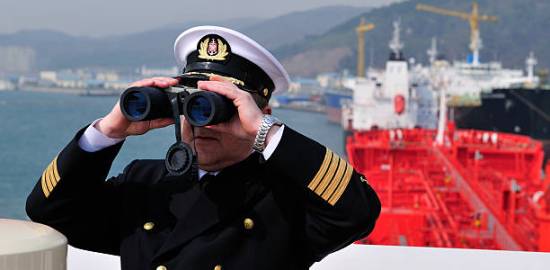 Navigation officer with binocular, looking ahead on the navigation bridge of ocean ship